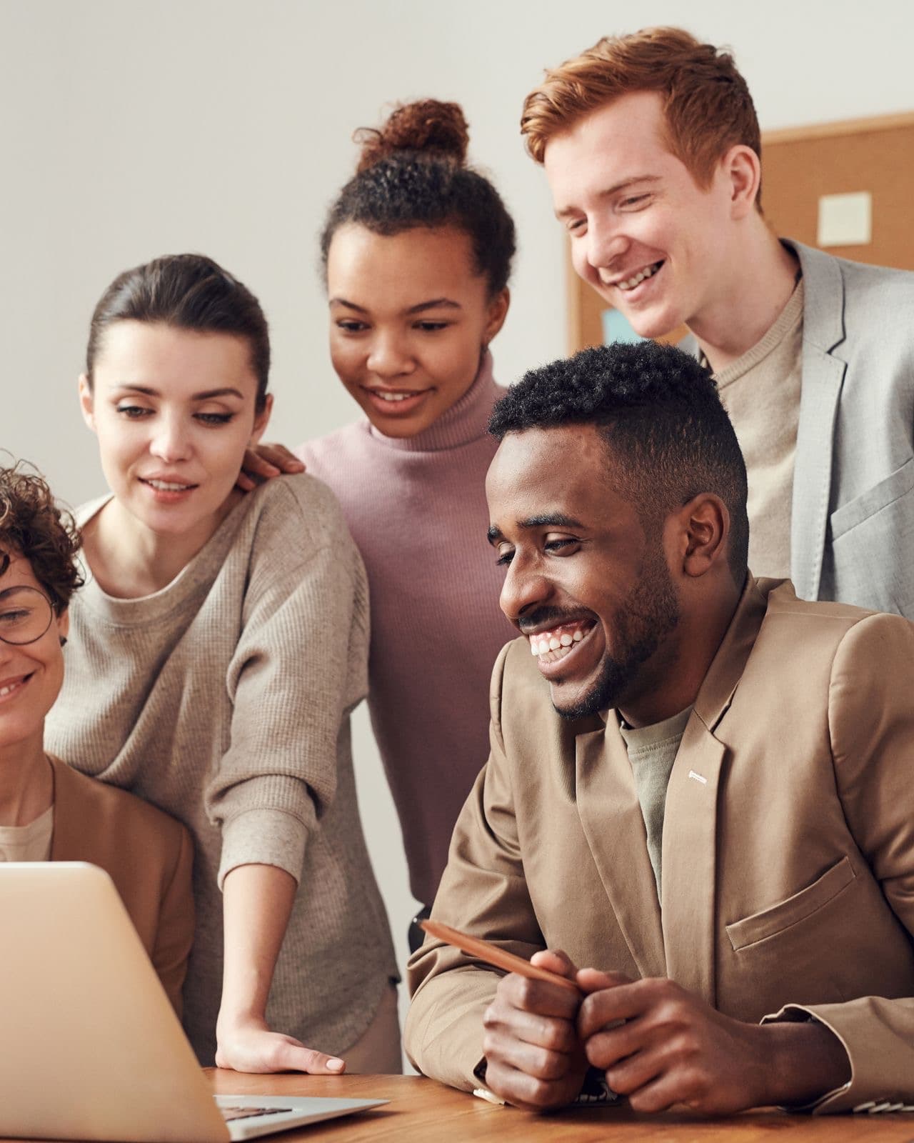 Colleagues gathered around a laptop at a shared desk, reviewing candidate information together