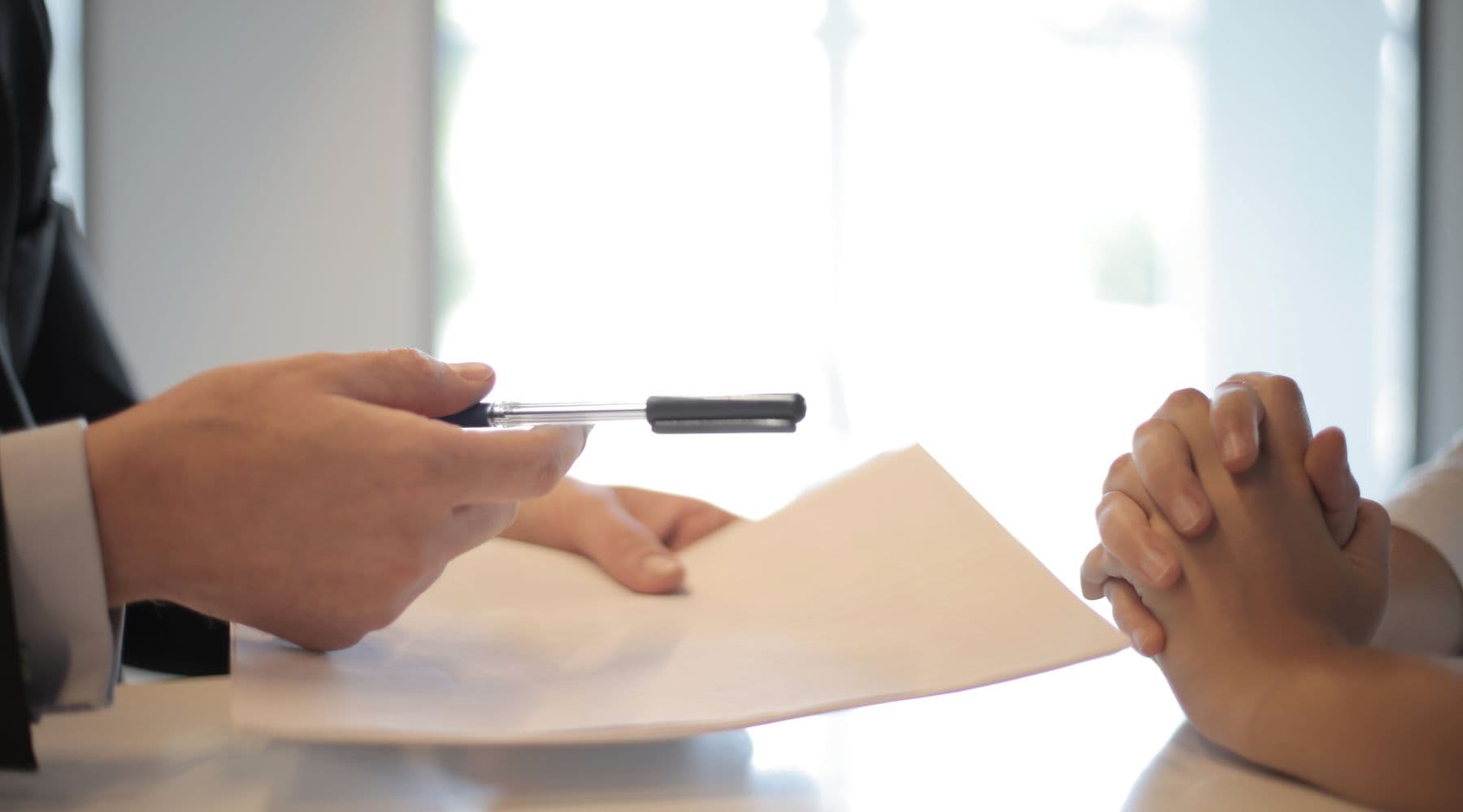 One person passing a document and pen across a desk to another